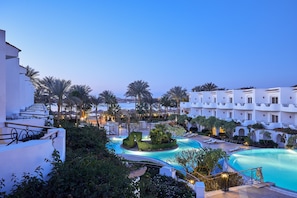 Een resort met een zwembad, palmbomen en witte gebouwen.
