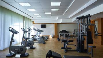 A gym with exercise equipment, a bench, and a wall-mounted TV.