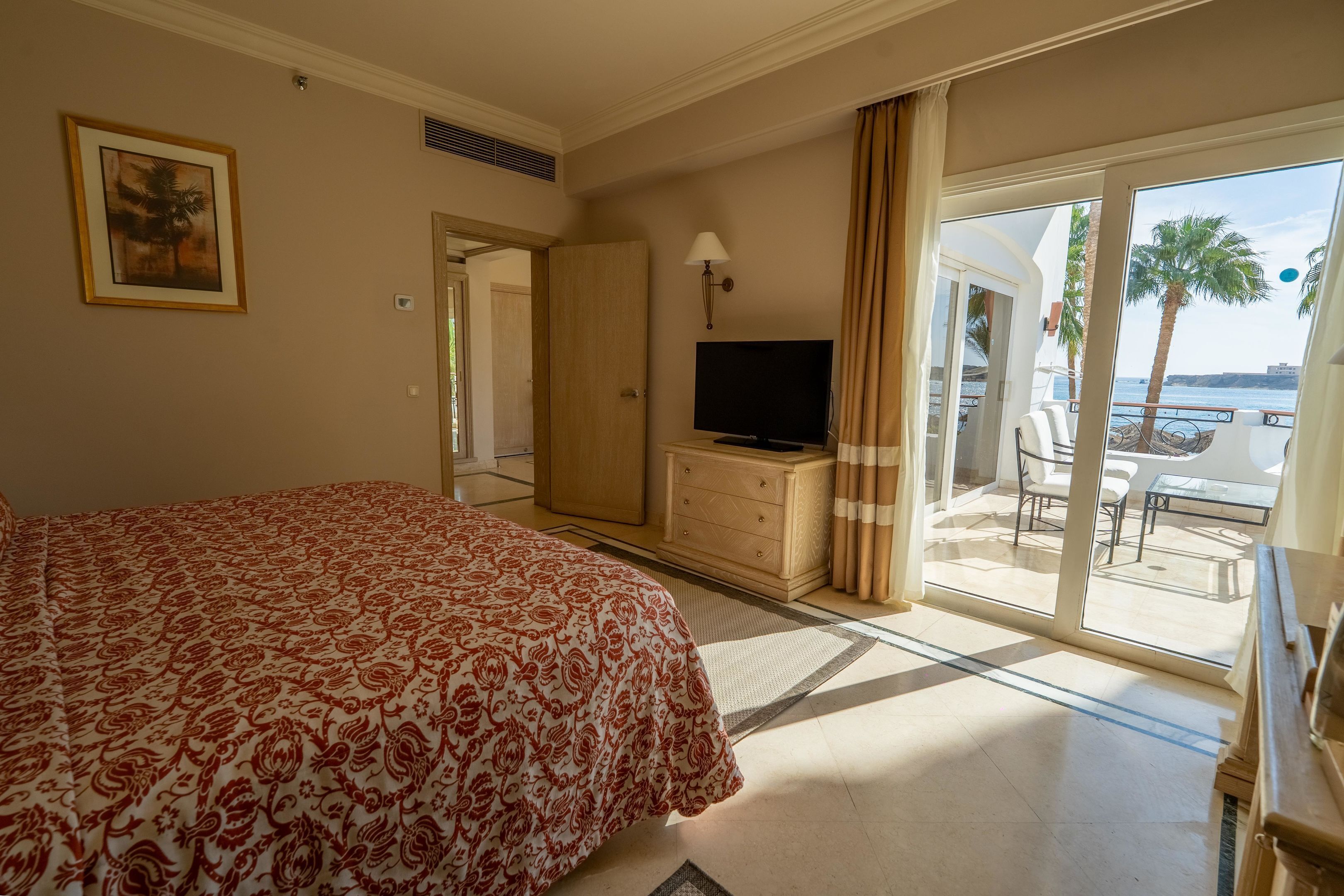 Ein Hotelzimmer mit Bett, Fernseher, Kommode und einem Balkon mit Meerblick.