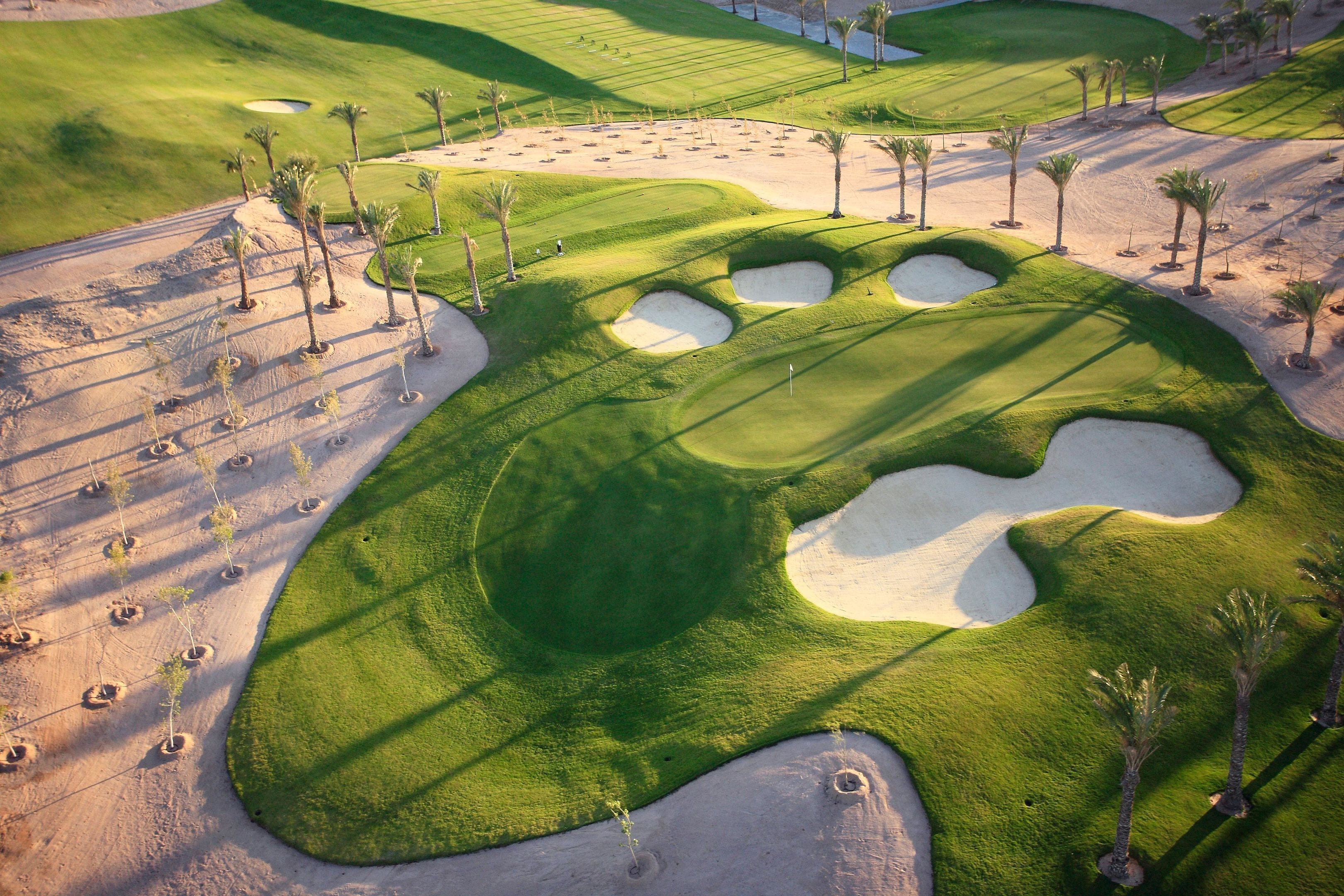A golf course with sand bunkers, palm trees, and a clear sky.