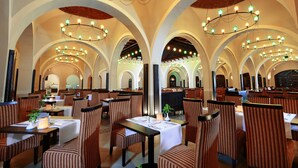Un restaurante con techos altos en arco, varias mesas de comedor y sillas tapizadas a rayas.