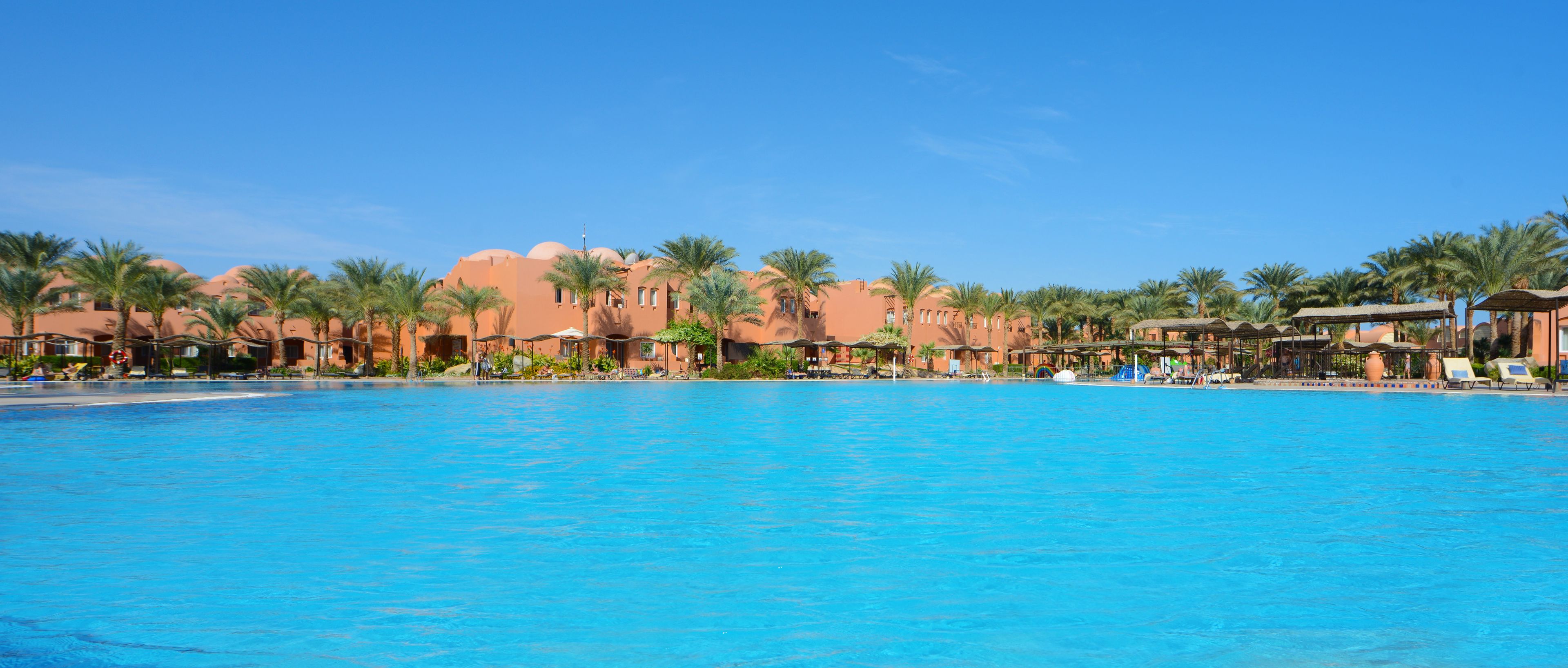 A resort with a large pool, palm trees, and Mediterranean-style buildings.