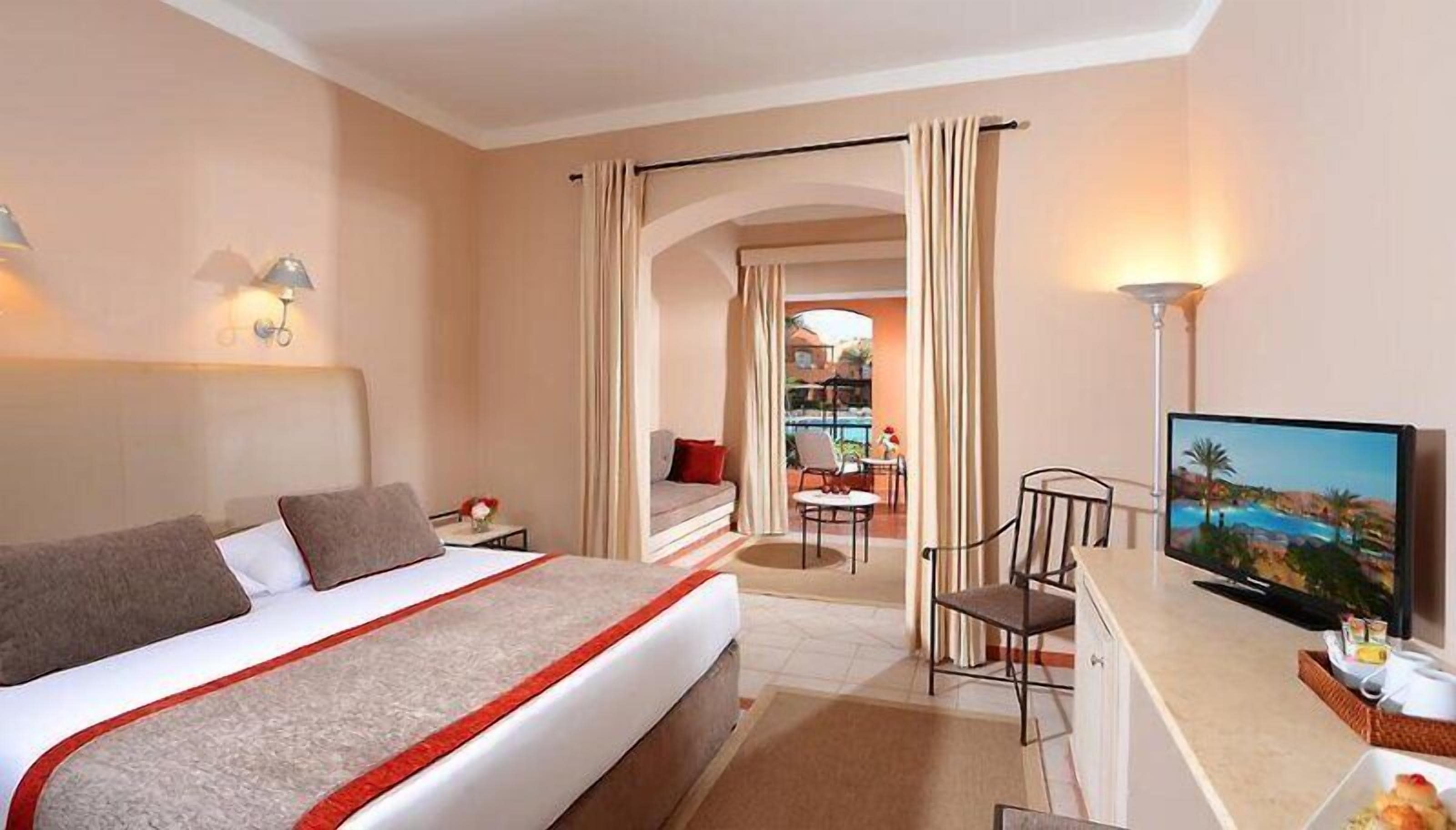 Ein Hotelzimmer mit Bett, Fernseher, Schreibtisch mit Stuhl und Blick auf einen Außenbereich.