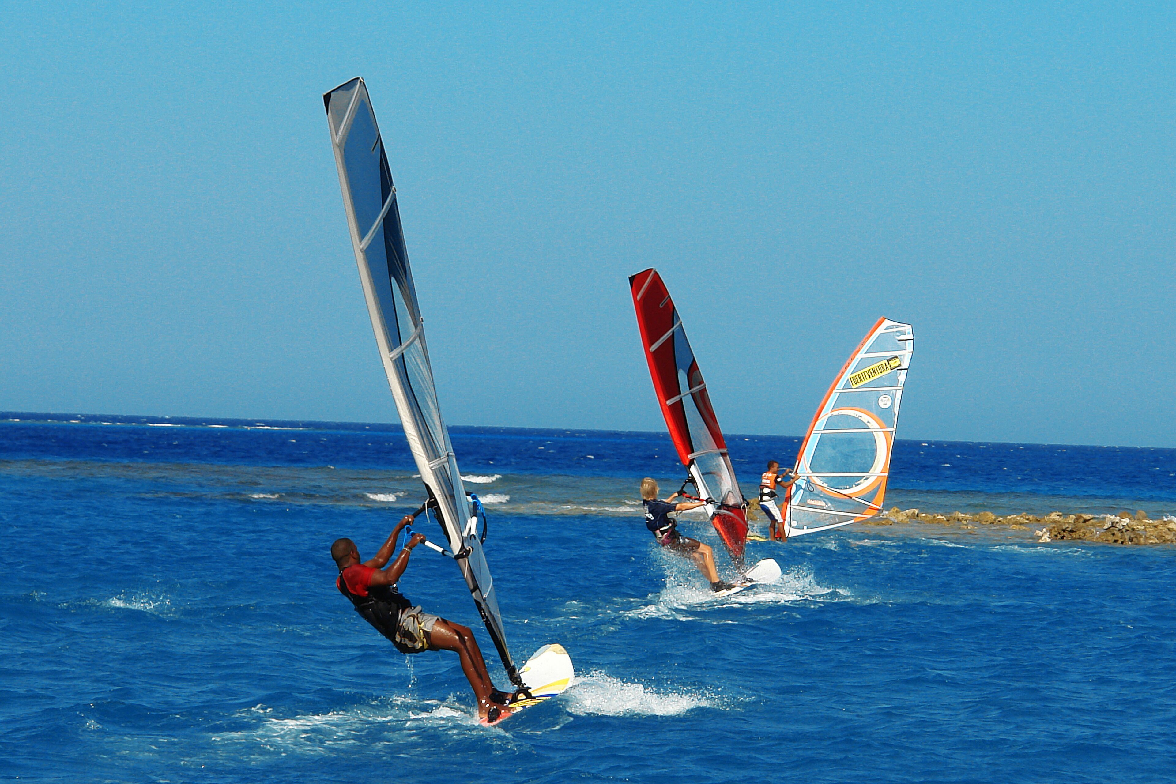 Trois personnes pratiquent la planche à voile sur une mer d’un bleu limpide.