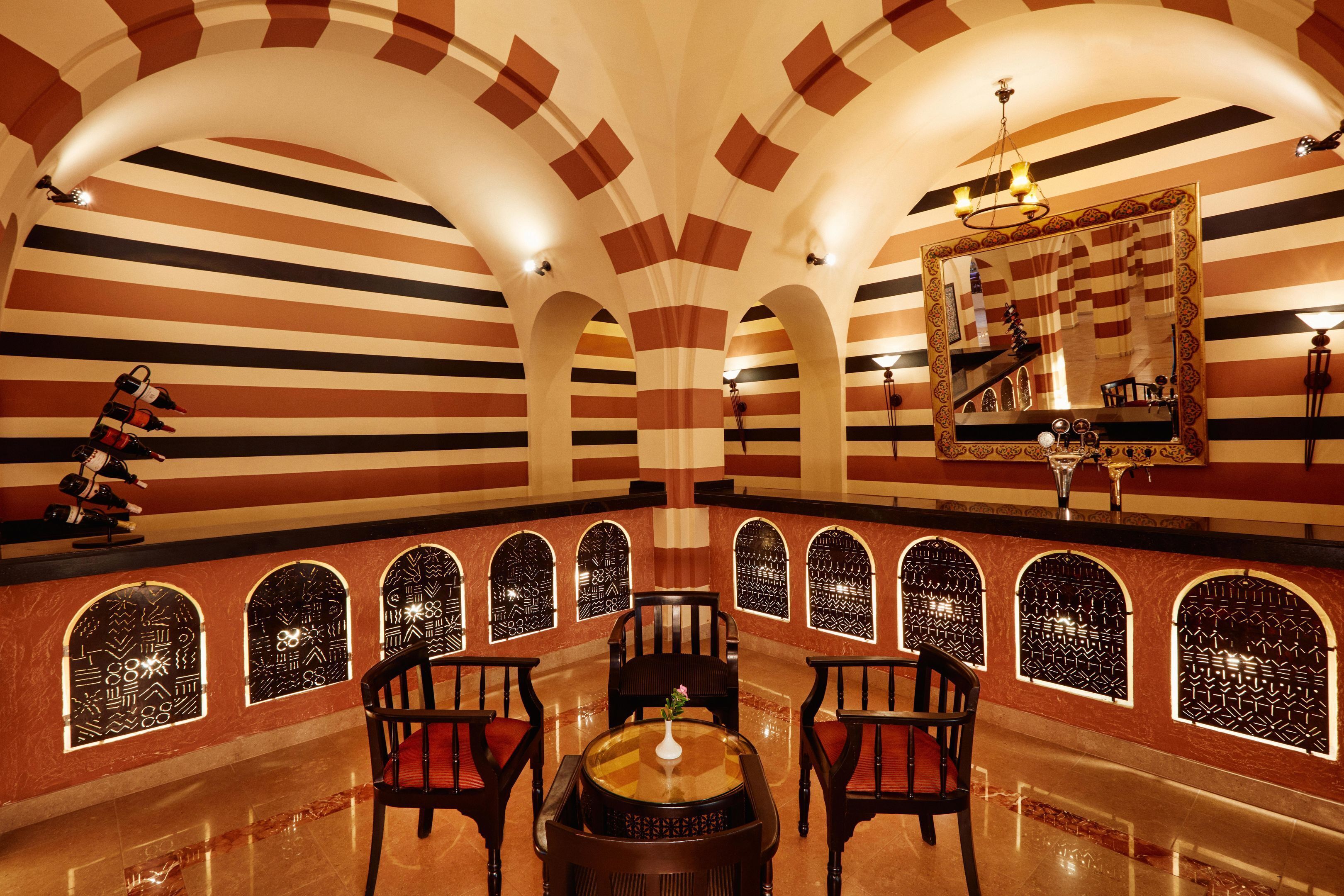 A room with striped walls, arched windows, a chandelier, and a table with chairs.