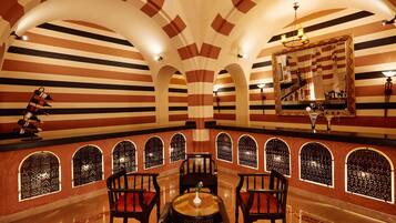 A room with striped walls, arched windows, a chandelier, and a table with chairs.
