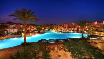 Piscina de un resort con palmeras, sillas de descanso y una iluminación nocturna.