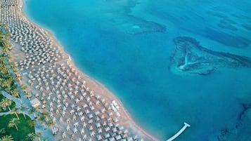 Vista aérea de una playa con numerosas sombrillas y sillas de playa, mar azul cristalino y embarcaciones en el agua.