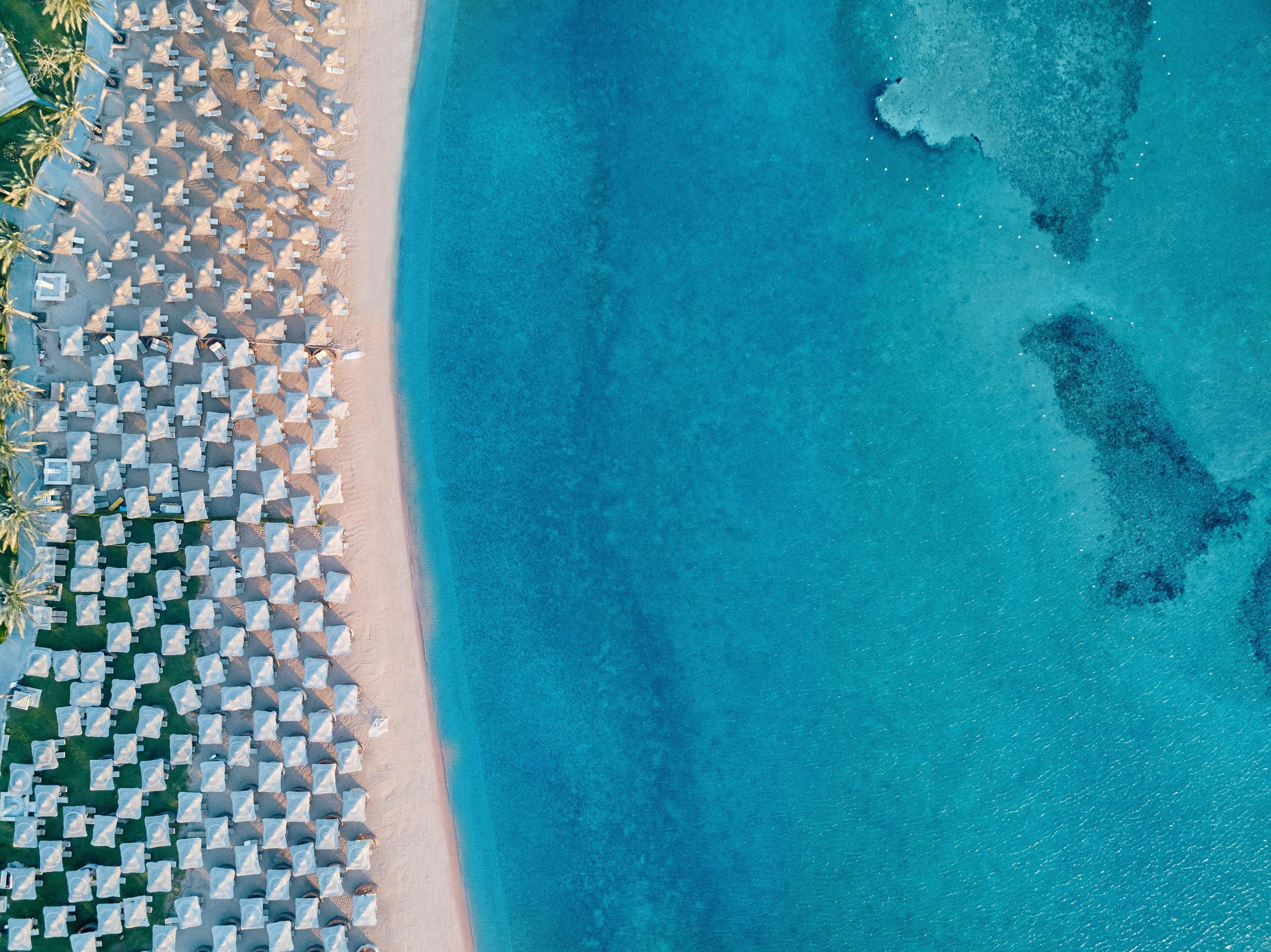 Vista aérea de una playa con hileras de sombrillas y sillas de playa blancas.