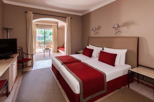 A hotel room with two beds, a TV, a desk, and a balcony with chairs.