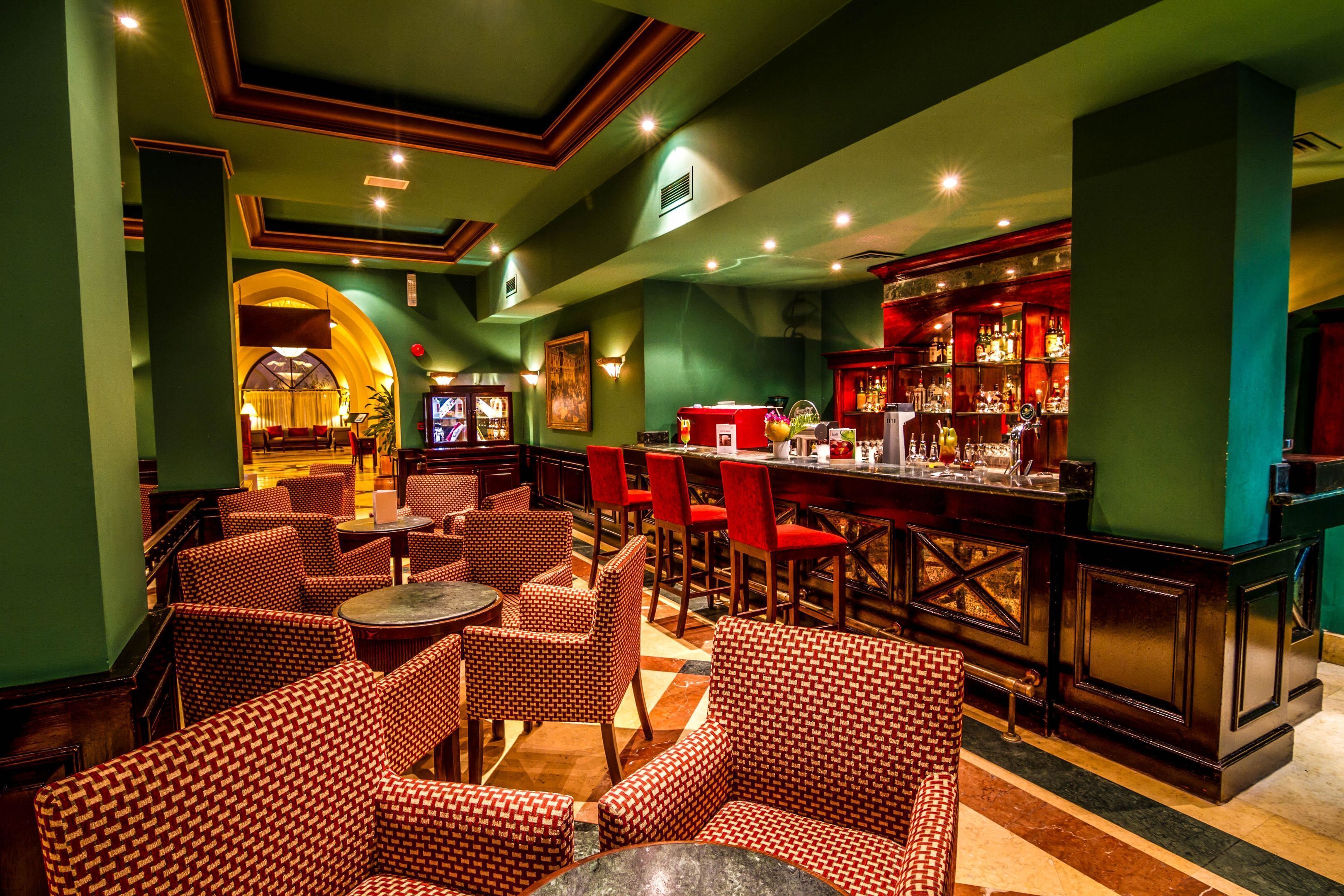 A bar area with red and white patterned chairs, a bar counter, and a green wall.