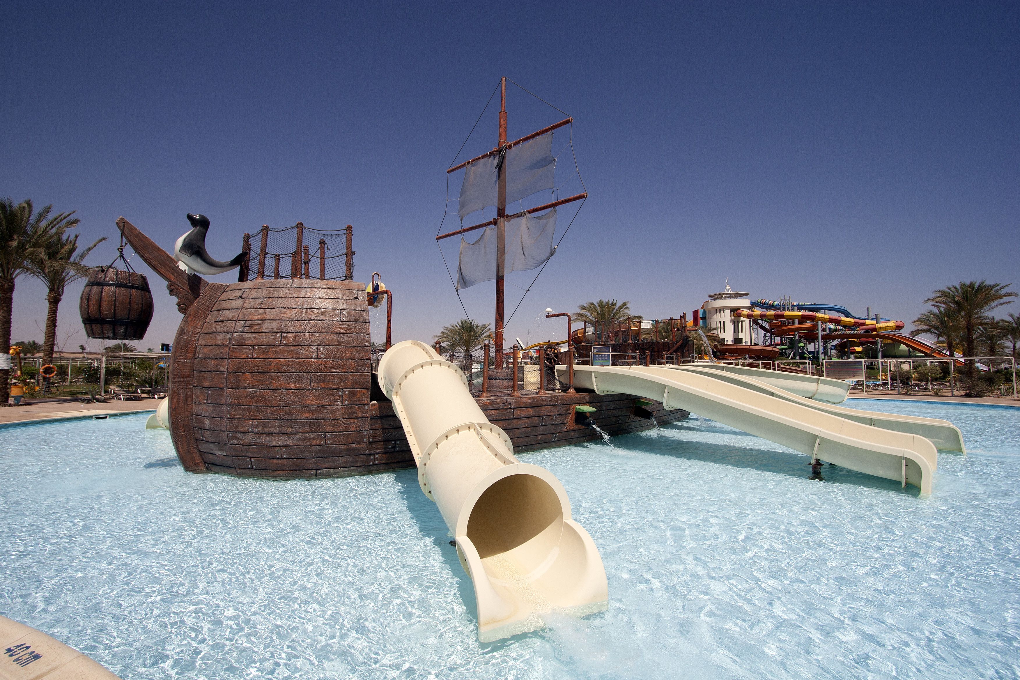 Un parque acuático con un tobogán de temática pirata, un barril de madera grande y un tobogán acuático de varios niveles.