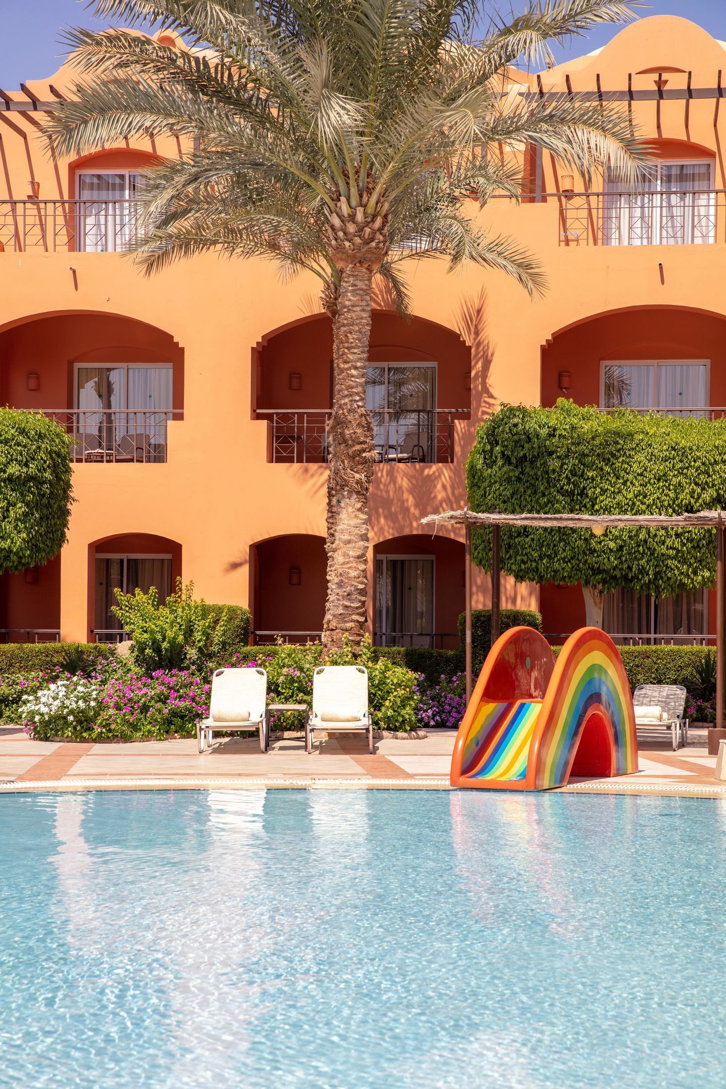 A hotel with a pool, palm trees, and a colorful play structure.