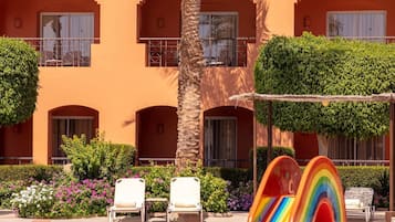 A hotel with a pool, palm trees, and a colorful play structure.