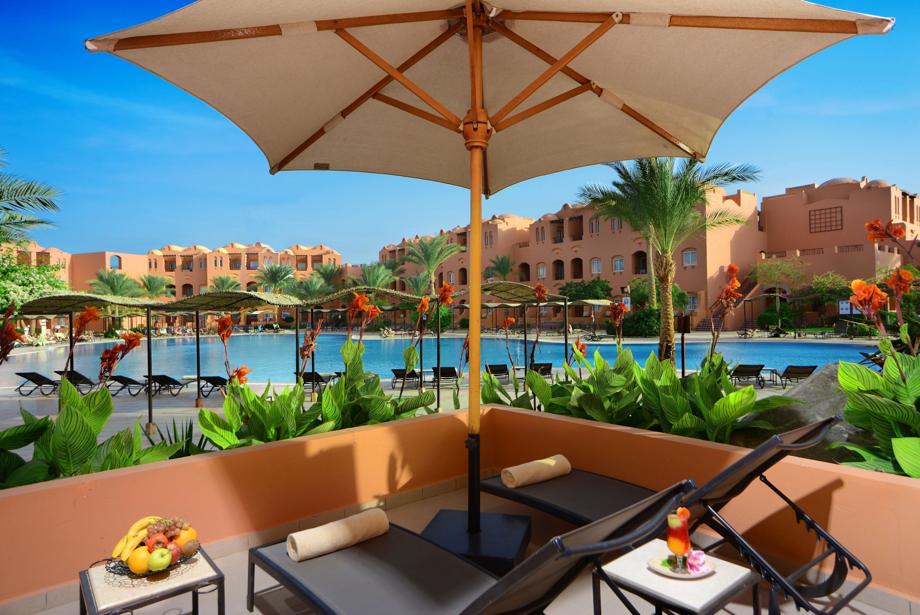 Un espace aménagé au bord de la piscine, avec des chaises longues, un parasol et un panier de fruits.