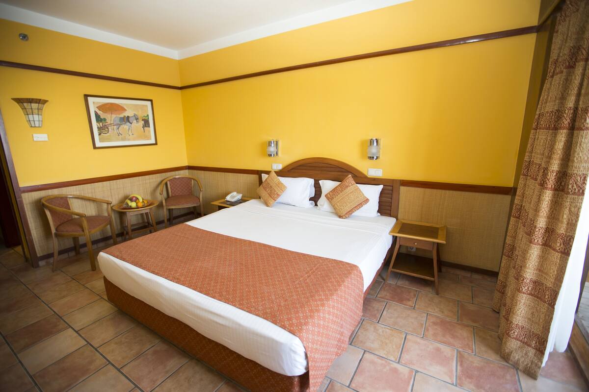 Une chambre d’hôtel avec un grand lit, un bureau avec une chaise, une petite table avec des fruits et un tableau au mur.