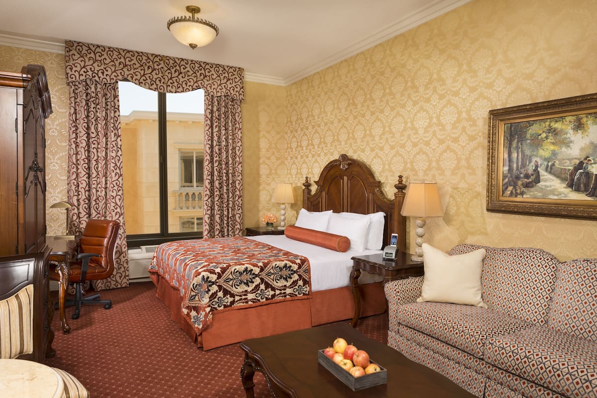 Een hotelkamer met een groot bed, een slaapbank, een bureau en een schilderij aan de muur.