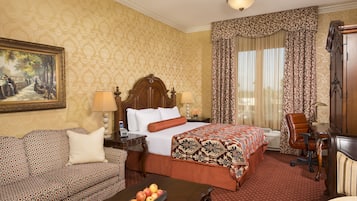 A hotel room with a large bed, a sofa, a desk, and a painting on the wall.