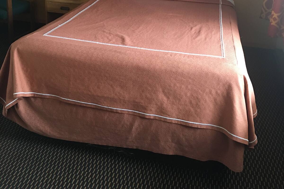 Una habitación de hotel con una cama bien hecha, una mesita de noche con una lámpara y una obra de arte enmarcada en la pared.