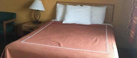 A hotel room with a neatly made bed, a nightstand with a lamp, and a framed artwork on the wall.