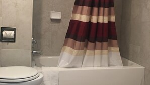 A bathroom with a white toilet, a bathtub, and a shower curtain with a striped pattern. - Caravan Motel (Niagara Falls)