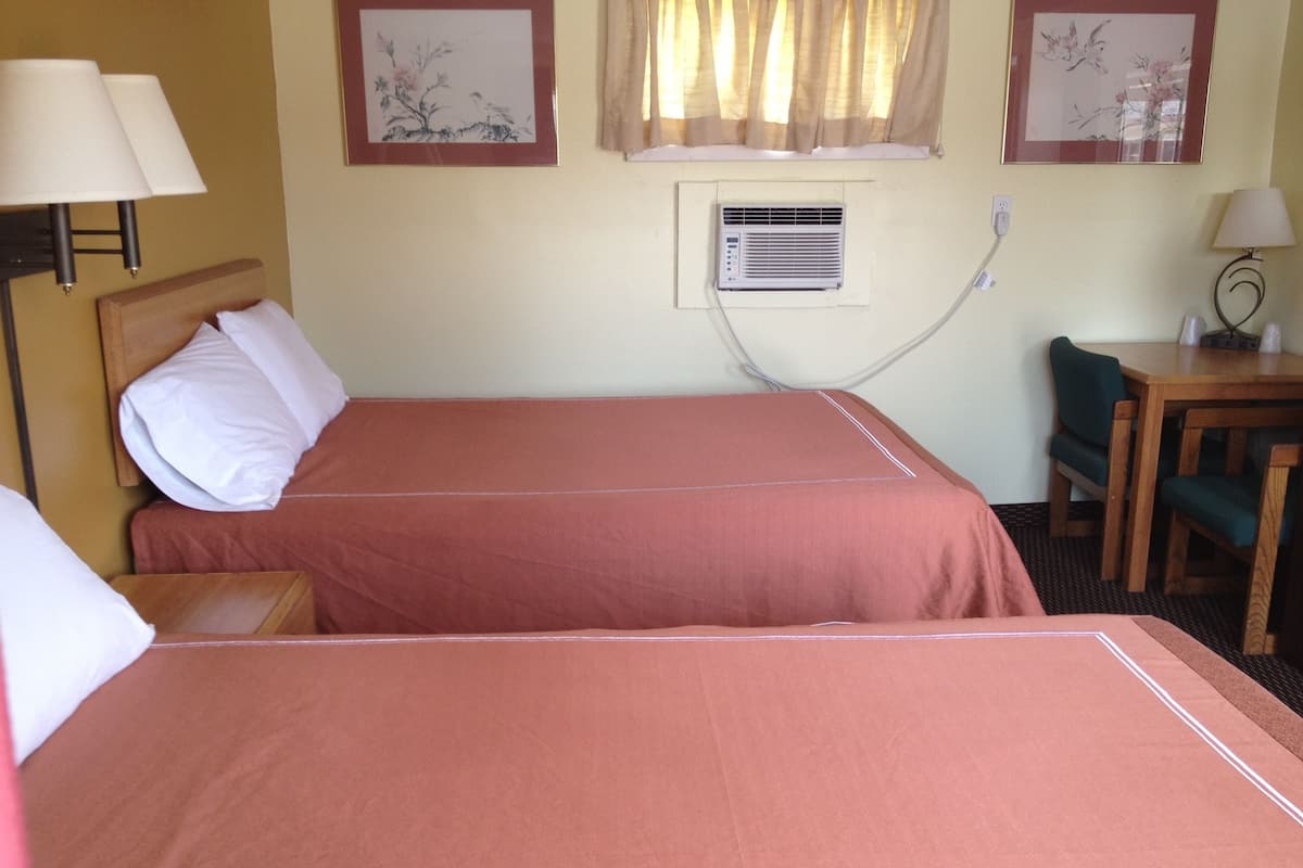 Habitación de hotel con dos camas, un escritorio, una silla y un equipo de aire acondicionado.