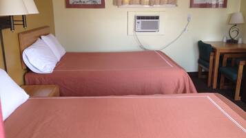 A hotel room with two beds, a desk, a chair, and an air conditioning unit.