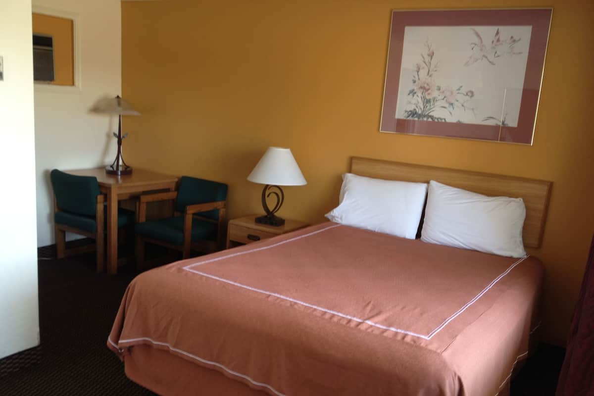 Habitación de hotel con una cama grande, un escritorio con silla, una lámpara y una obra de arte enmarcada en la pared.