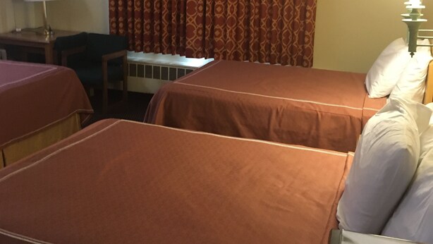 A hotel room with two beds, a desk, a chair, a television, and a lamp. - Caravan Motel (Niagara Falls)