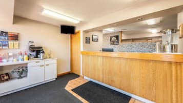 Zona de recepción de un hotel con mostrador de madera, una pequeña cocina y piso de baldosas.