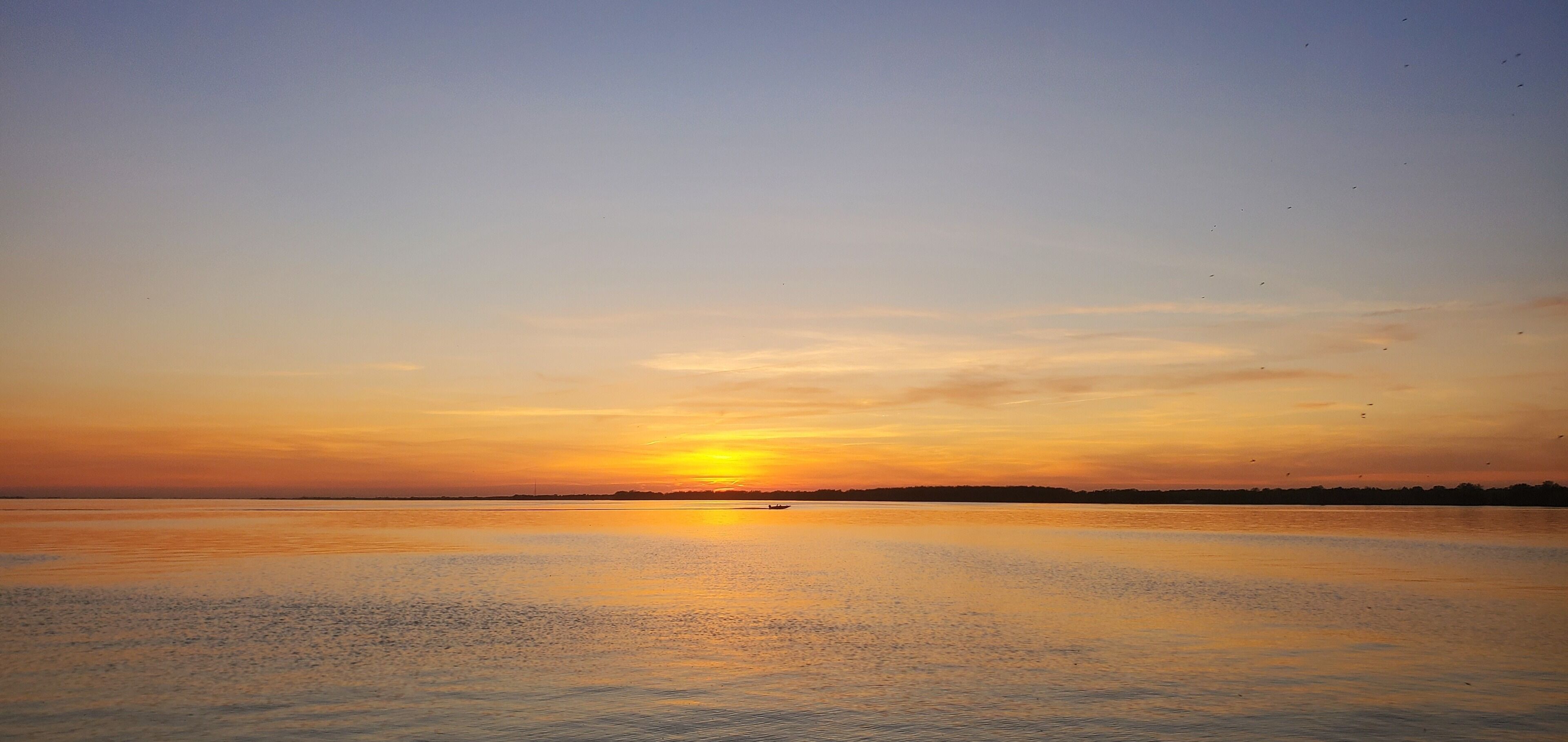 A calm body of water reflecting a sunset with a clear sky.