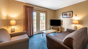 A hotel room with a sofa, a television, a small table, and a lamp.