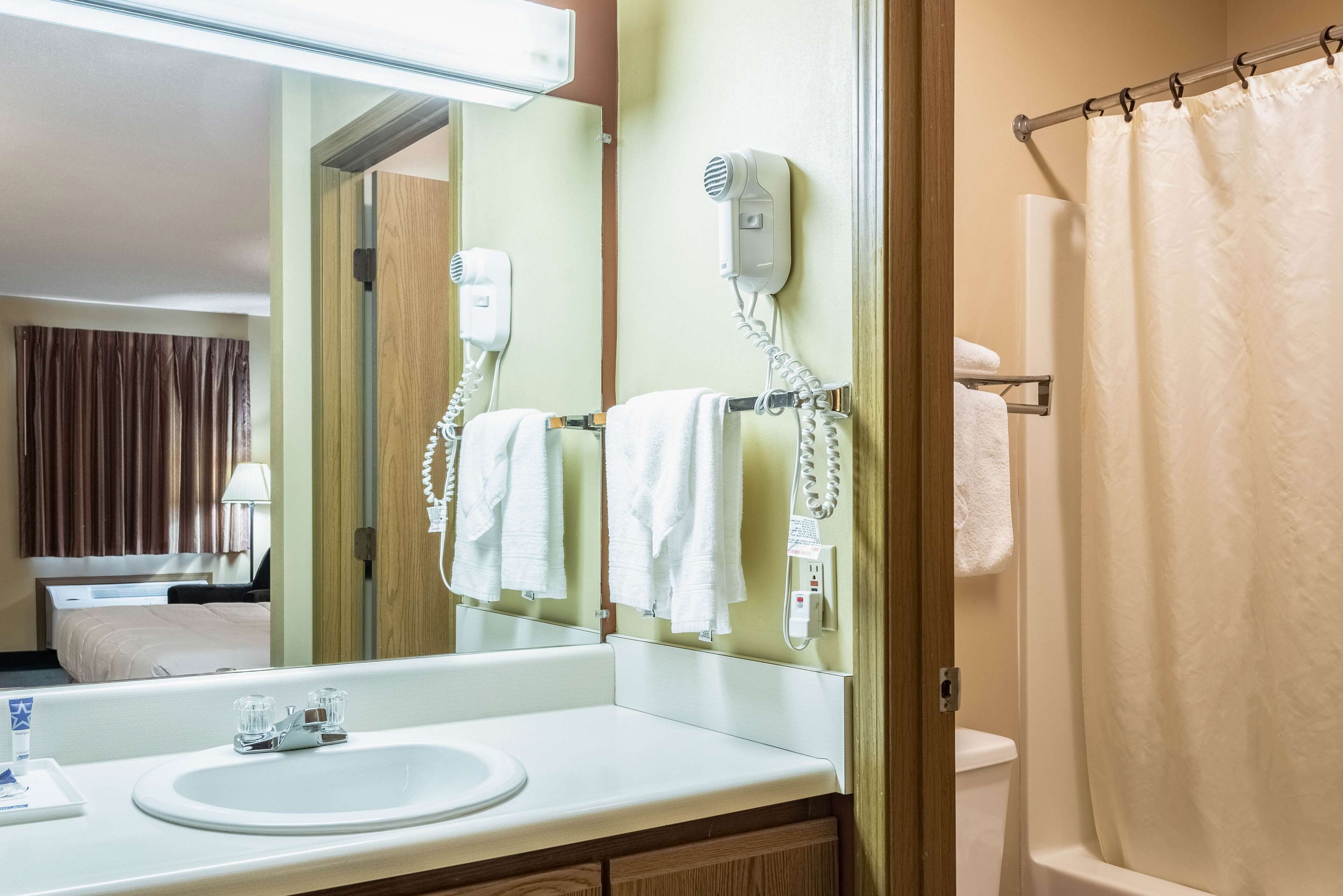 A hotel bathroom with a sink, mirror, hair dryer, towel rack, and shower curtain.