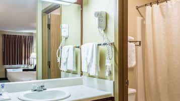 Un baño de hotel con lavamanos, espejo, secador de pelo, toallero y cortina de ducha.