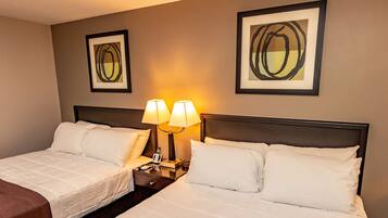 A hotel room with two beds, a nightstand with lamps, and two framed abstract paintings on the wall.