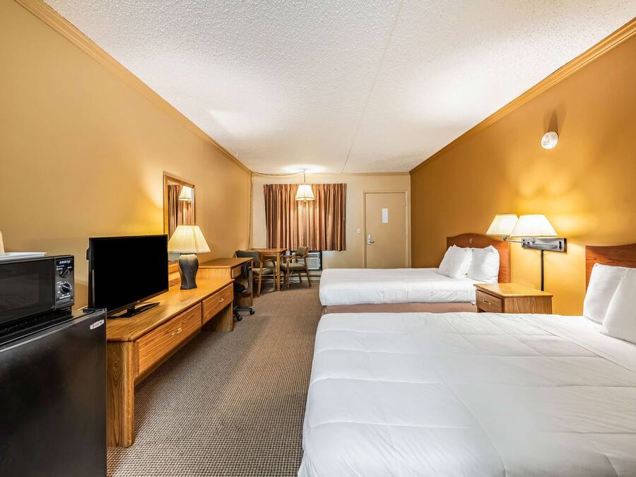 A hotel room with two beds, a desk with a TV, a refrigerator, and a lamp.
