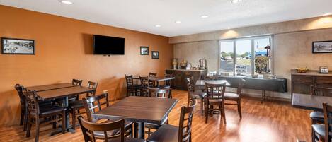 A spacious dining area with multiple tables and chairs, a flat-screen TV mounted on the wall, and a large window providing a view of the outside.