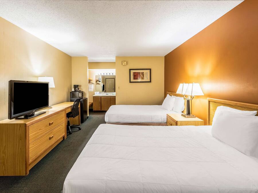 A hotel room with two beds, a TV, a desk, and a lamp.