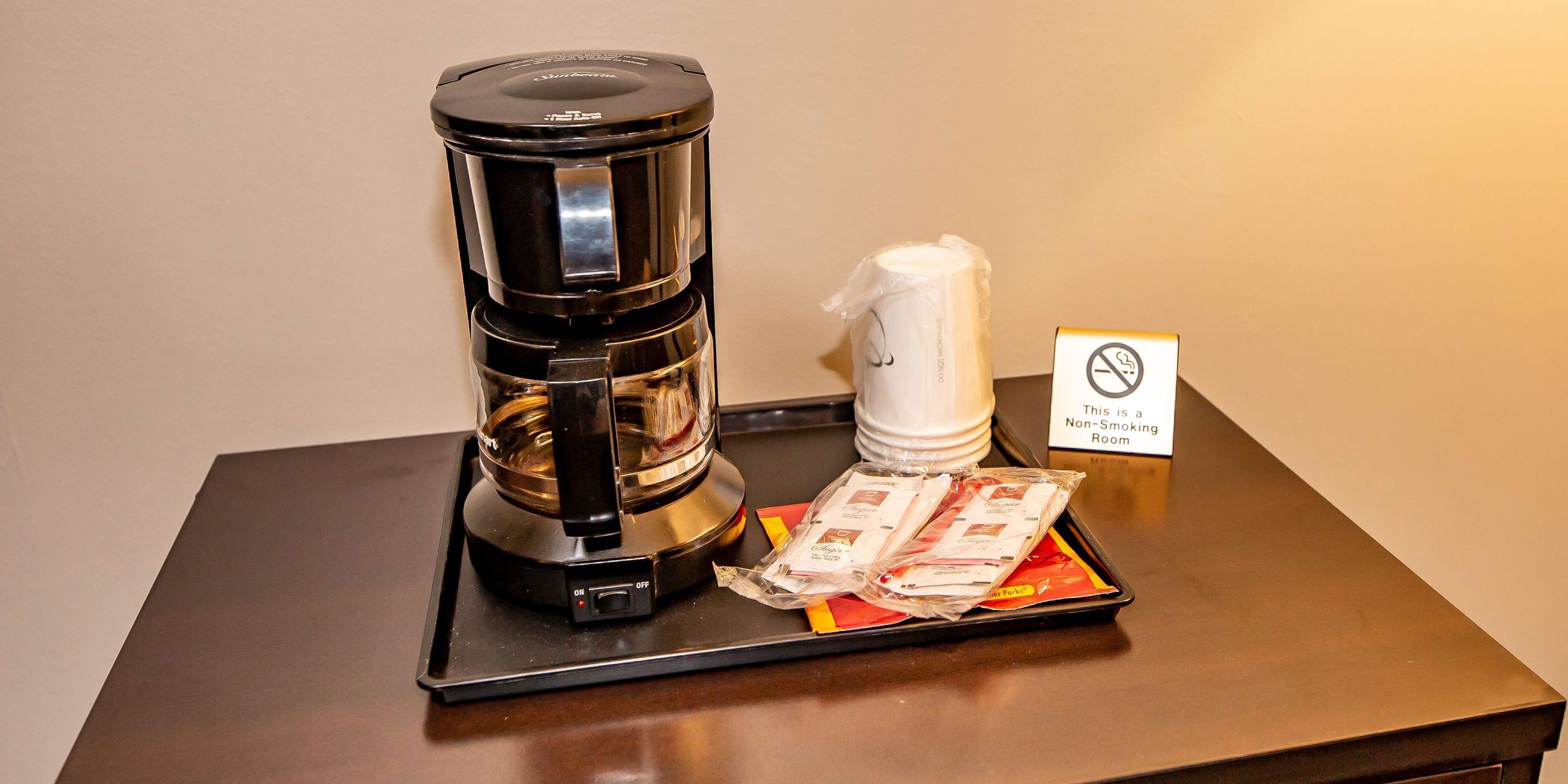 A coffee maker, a disposable coffee cup, and packets of sugar and creamer on a tray.