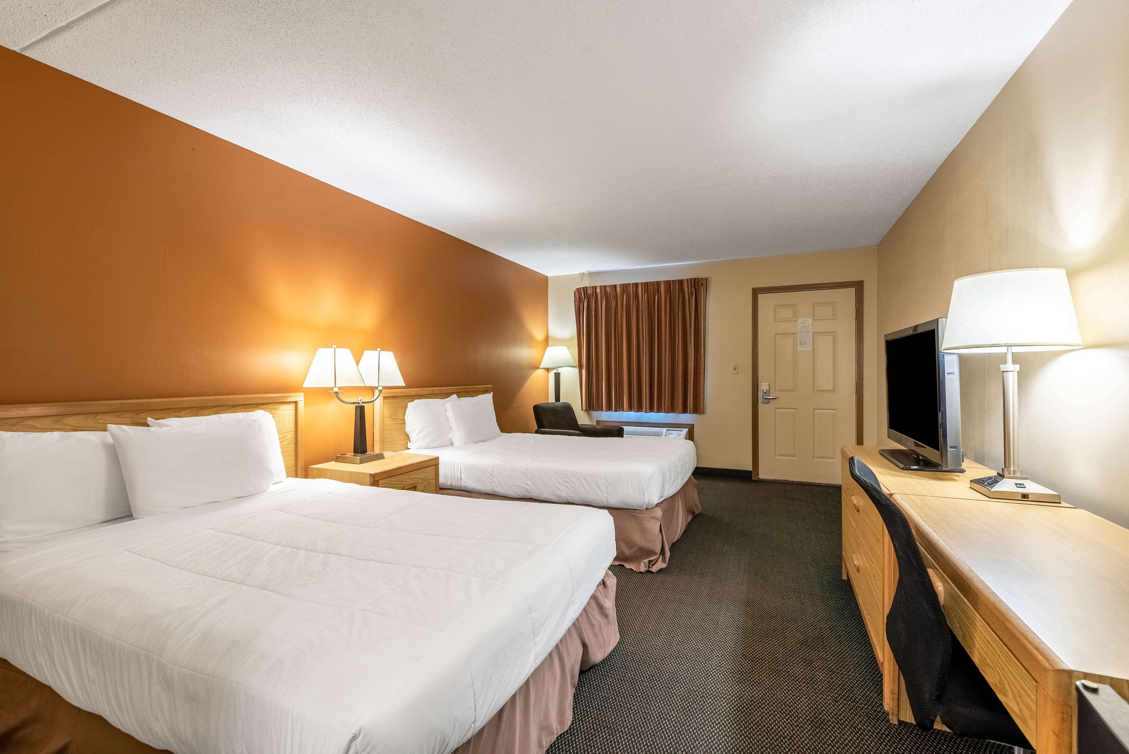 Ein Hotelzimmer mit zwei Betten, einem Schreibtisch, einem Fernseher und zwei Lampen.