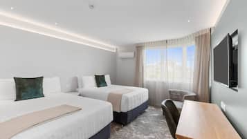Ein Hotelzimmer mit zwei Betten, einem Schreibtisch, einem Sessel, einem Fernseher und einem Fenster mit Vorhängen.