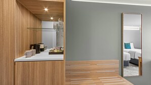 Una habitación de hotel moderna con una pared decorativa de madera, un estante de vidrio con artículos de aseo, una cama con almohada azul y un espejo grande.