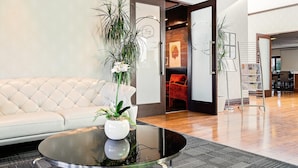 Un moderno vestíbulo con un sofá blanco capitonado, una mesa de centro de cristal con una planta y un mostrador de recepción de madera.