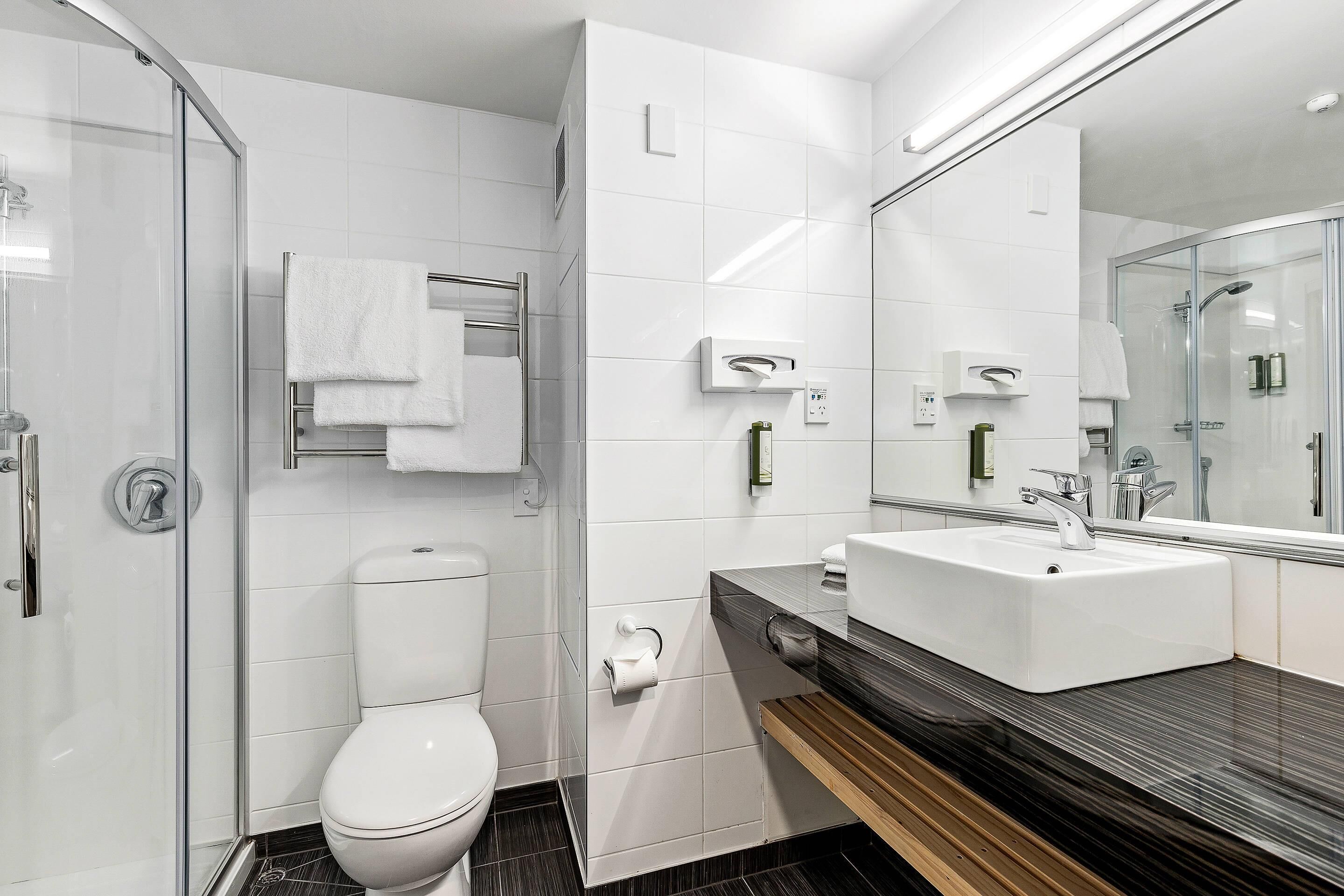 A modern bathroom with a glass shower enclosure, a white toilet, a sink with a mirror, and a towel rack.