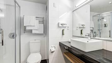 A modern bathroom with a glass shower enclosure, a white toilet, a sink with a mirror, and a towel rack.