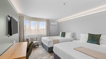 Quarto de hotel com duas camas, uma escrivaninha, uma cadeira e uma televisão.