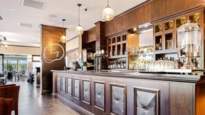 Zona de bar con mostrador de madera, taburetes y una variedad de botellas y vasos.