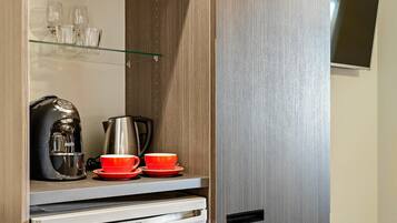 Una kitchenette con cafetera, hervidor y tazas rojas en un estante.