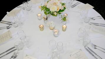 A round table set for a formal event with white tablecloths, glassware, and floral centerpieces.