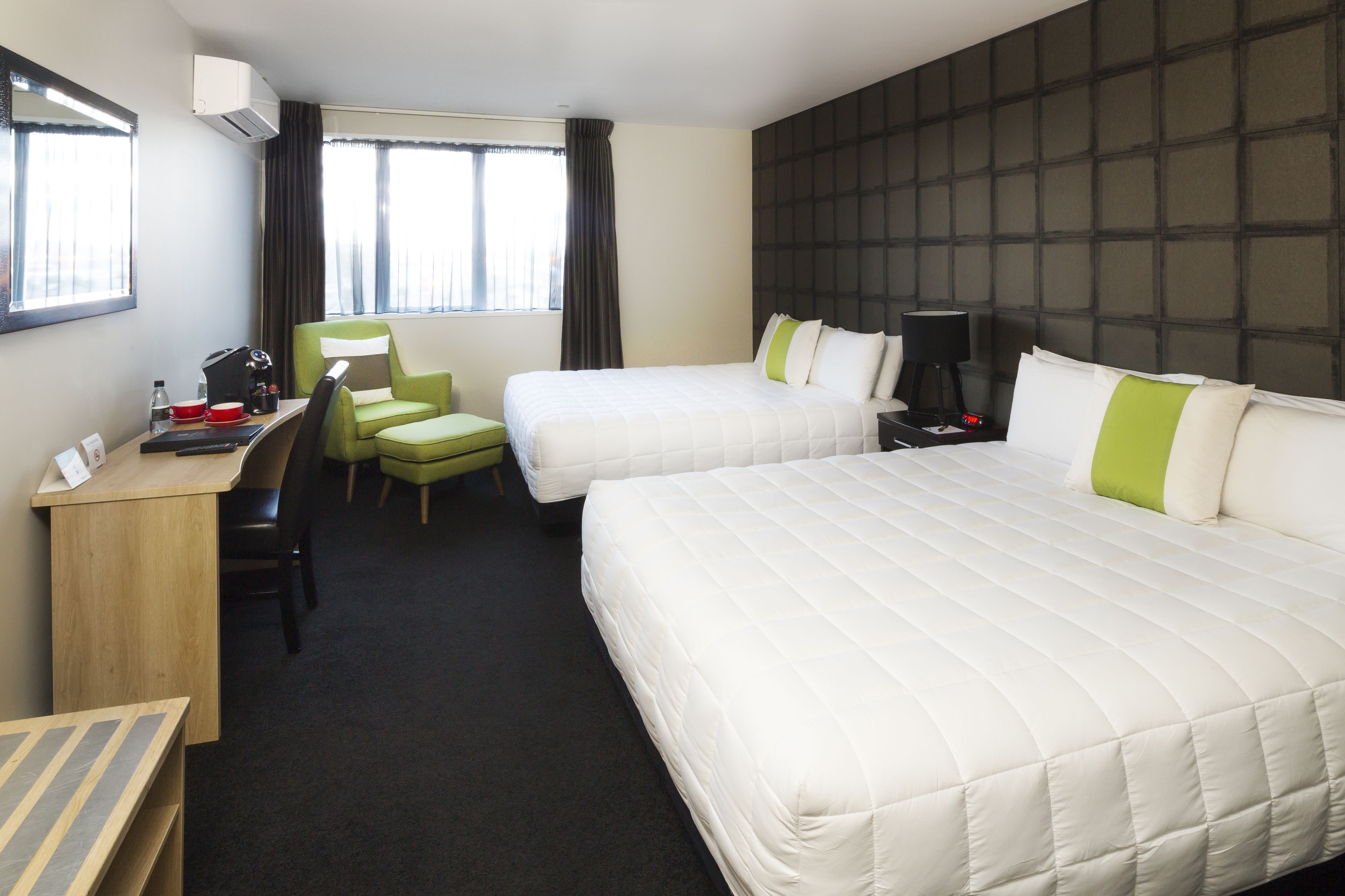 Una habitación de hotel con dos camas, un escritorio, una silla y un ventanal con cortinas.